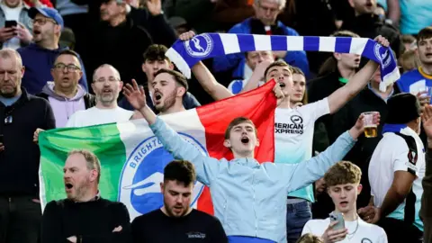 Getty Images Supporters of Brighton & Hove Albion during the UEFA Europa Round of 16 first leg match between AS Roma and Brighton & Hove Albion at Stadio Olimpico on 7 March 2024 in Rome, Italy. Supporters have their arms in the air and appear to be chanting.