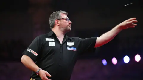 Getty Images James Wade of England throws against Luke Humphries of England during the 2024 Betfred World Matchplay semi-finals at Winter Gardens on July 20, 2024 in Blackpool, England.