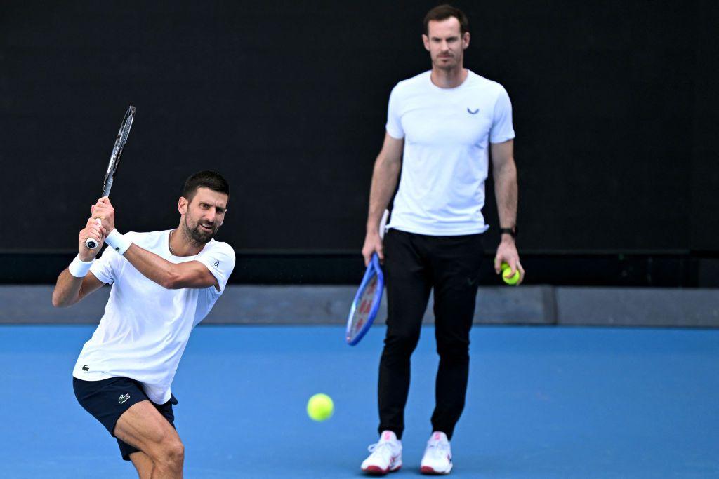 Novak Djokovic plays a backhand while practising at Melbourne Park with Andy Murray watching behind him