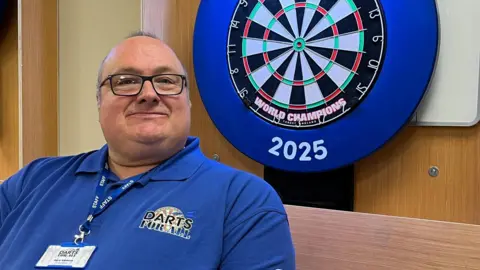 BBC Gary Siddons, at the John Storer House, where the first session of Darts for All took place. He is next to a darts board which moves vertically.