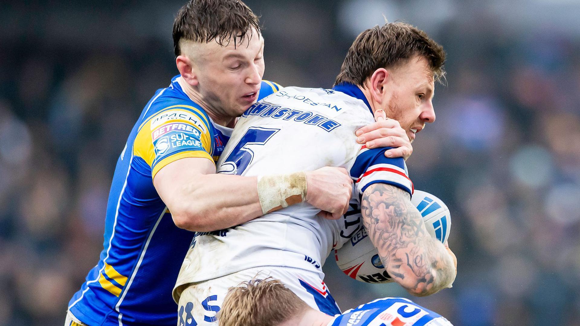 Wakefield winger Tom Johnstone is tackled high around the chest by Leeds centre Harry Newman as he tries to seek support with the ball tucked under his arm