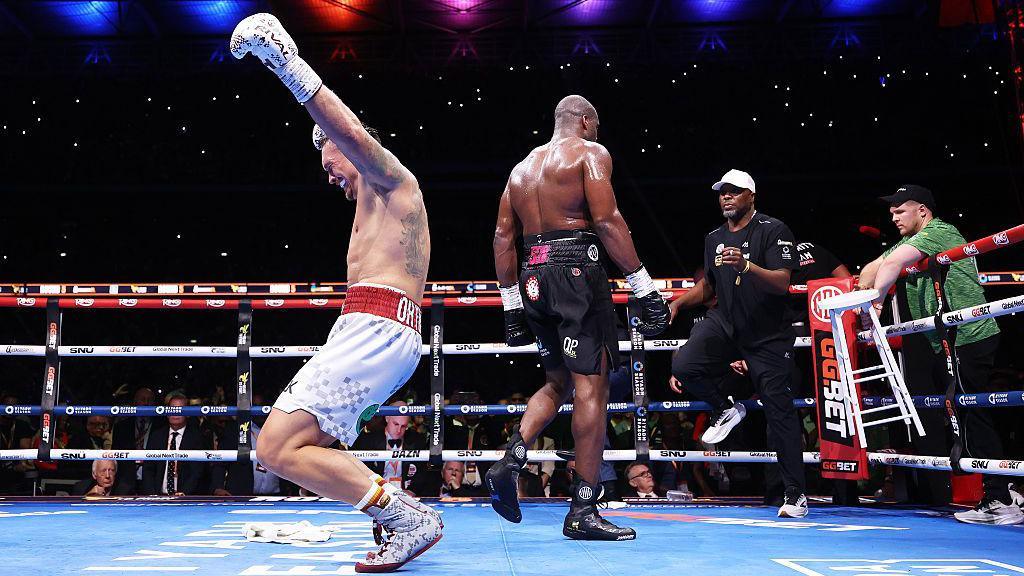 Oleksandr Usyk sinks to his knees celebrating as Daniel Dubois walks back to his corner