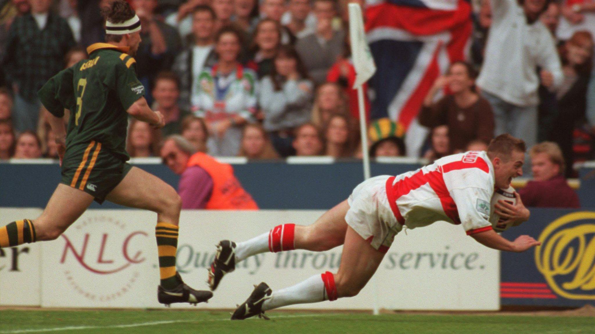 Paul Newlove dives over the line to score for England at Wembley, as Australia centre Mark Coyne watches on helplessly. Fans cheer in the background knowing England are ahead.