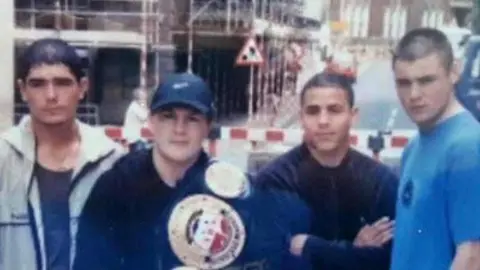 Thomas McDonagh A dated photograph of Ricky Hatton with a championship belt draped over his shoulder posing with three other male boxers on a street. They're standing in casual clothing in front of a building site with scaffolding.