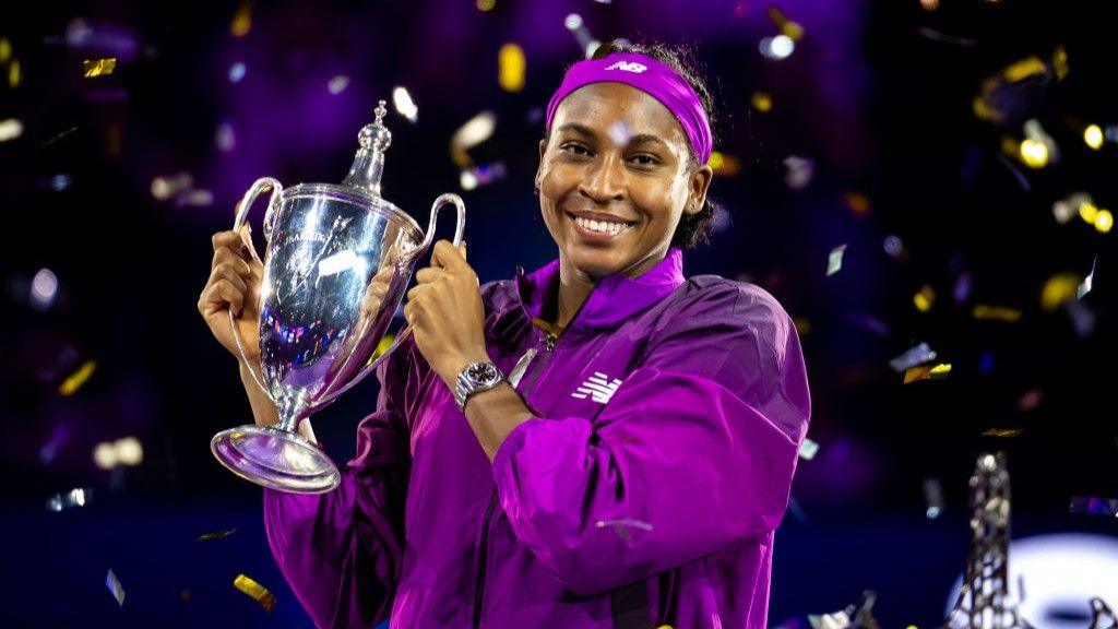 Coco Gauff smiles and holds up the Billie Jean King Trophy